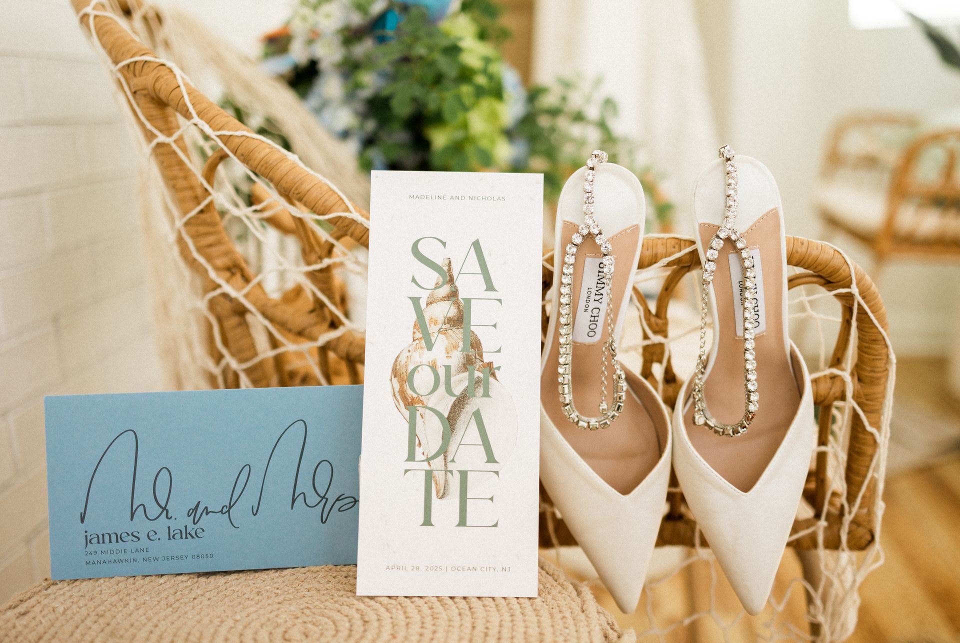 Wedding details: invitation, Save the Date card, and white jeweled heels on a woven chair.