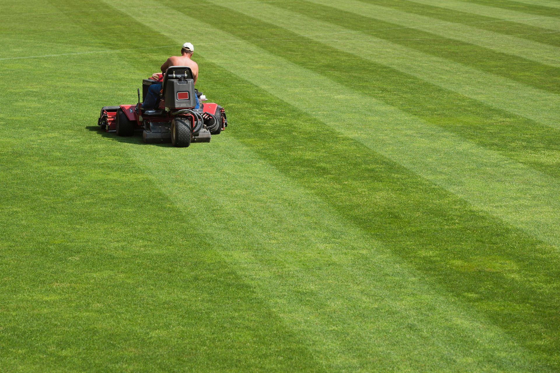 Person mowing a striped green lawn on a riding mower