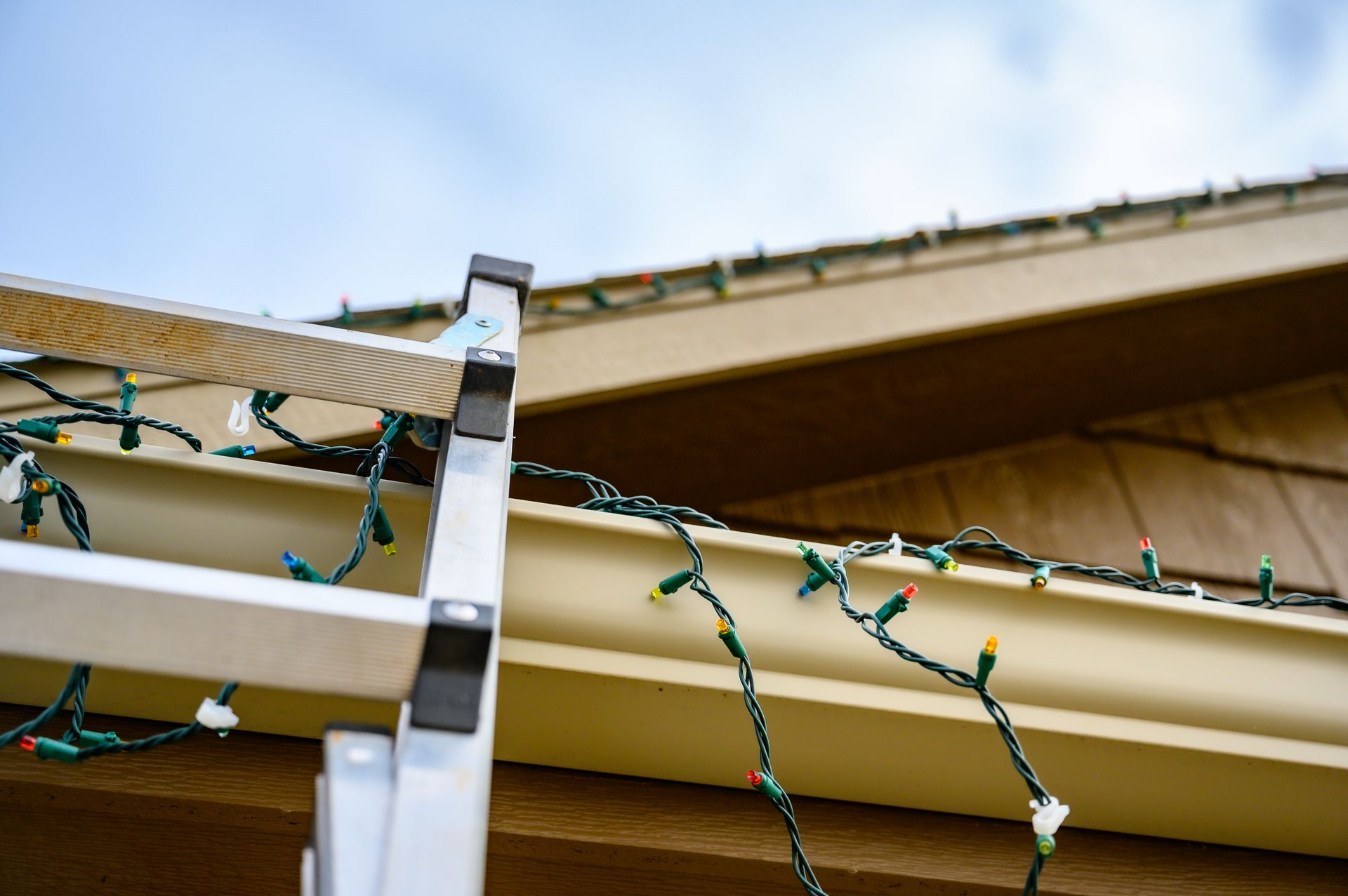 Ladder propped against a roof edge with tangled green string lights along the gutter