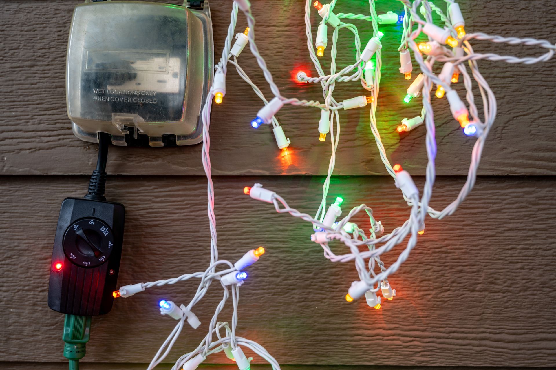 LED string lights and a small battery pack on a wooden surface, with multicolored lights glowing nearby