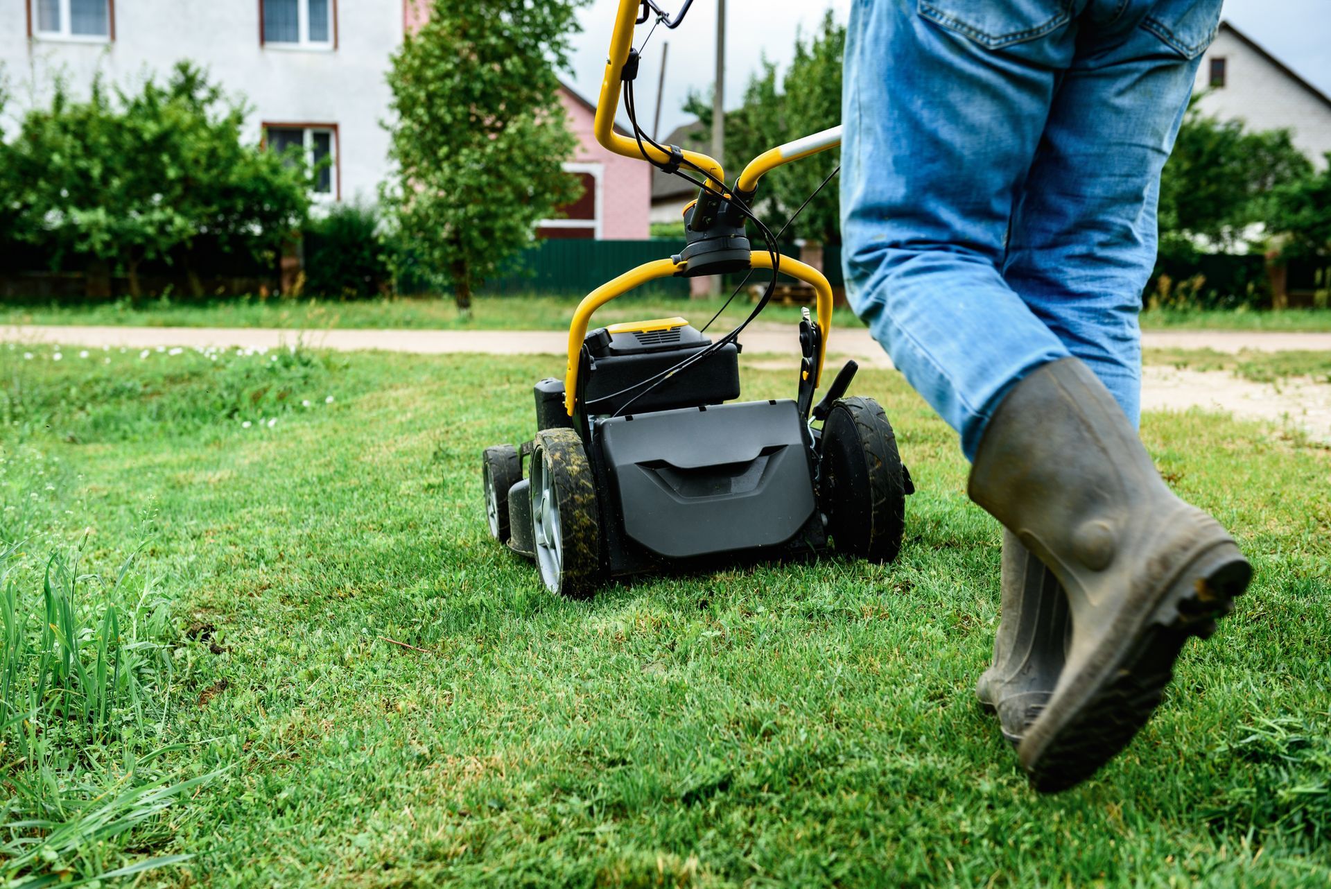 Person pushing a small black and yellow lawn mower across a grassy yard