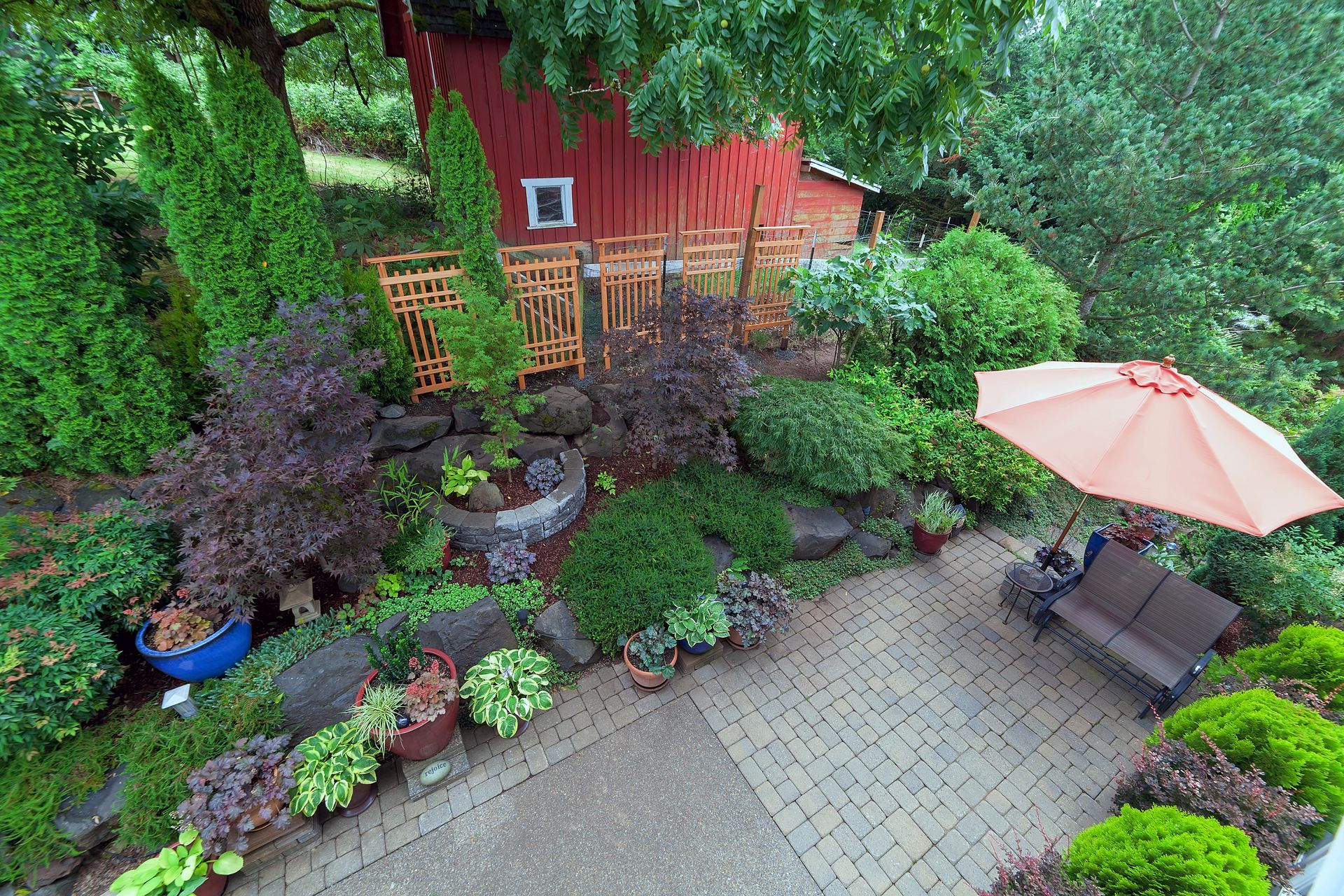 Backyard patio with lush garden beds, red shed, and a beige patio umbrella
