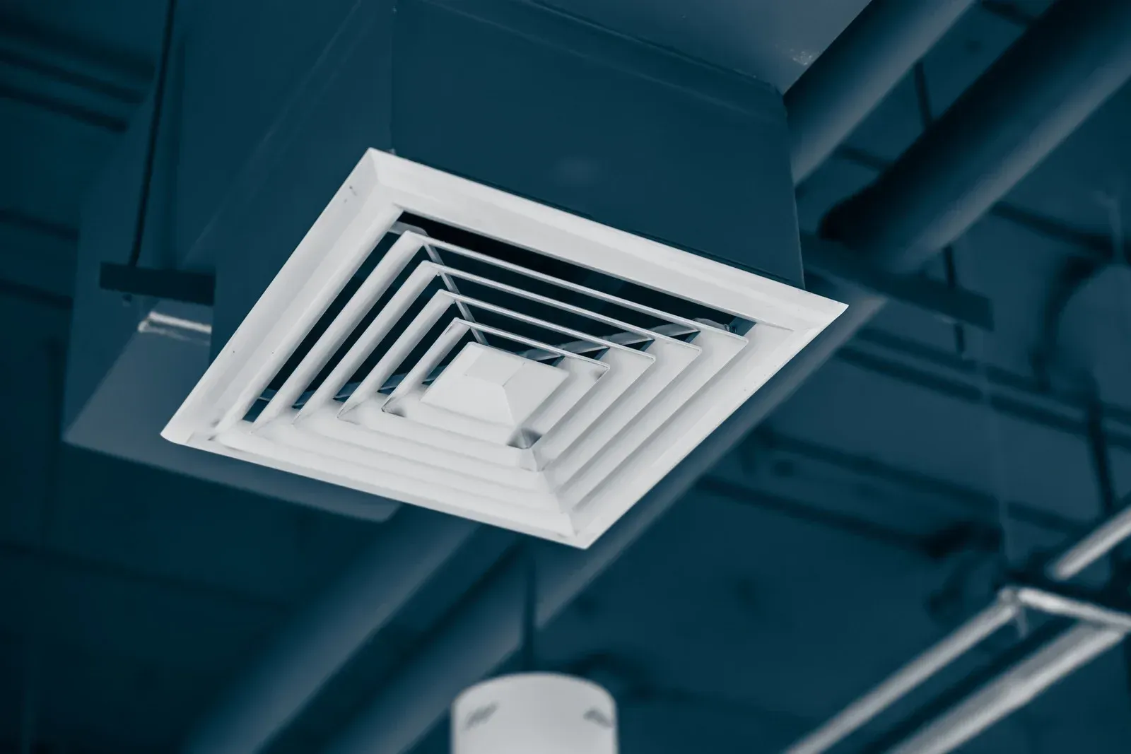 White ceiling air vent against a blue industrial ceiling with exposed pipes