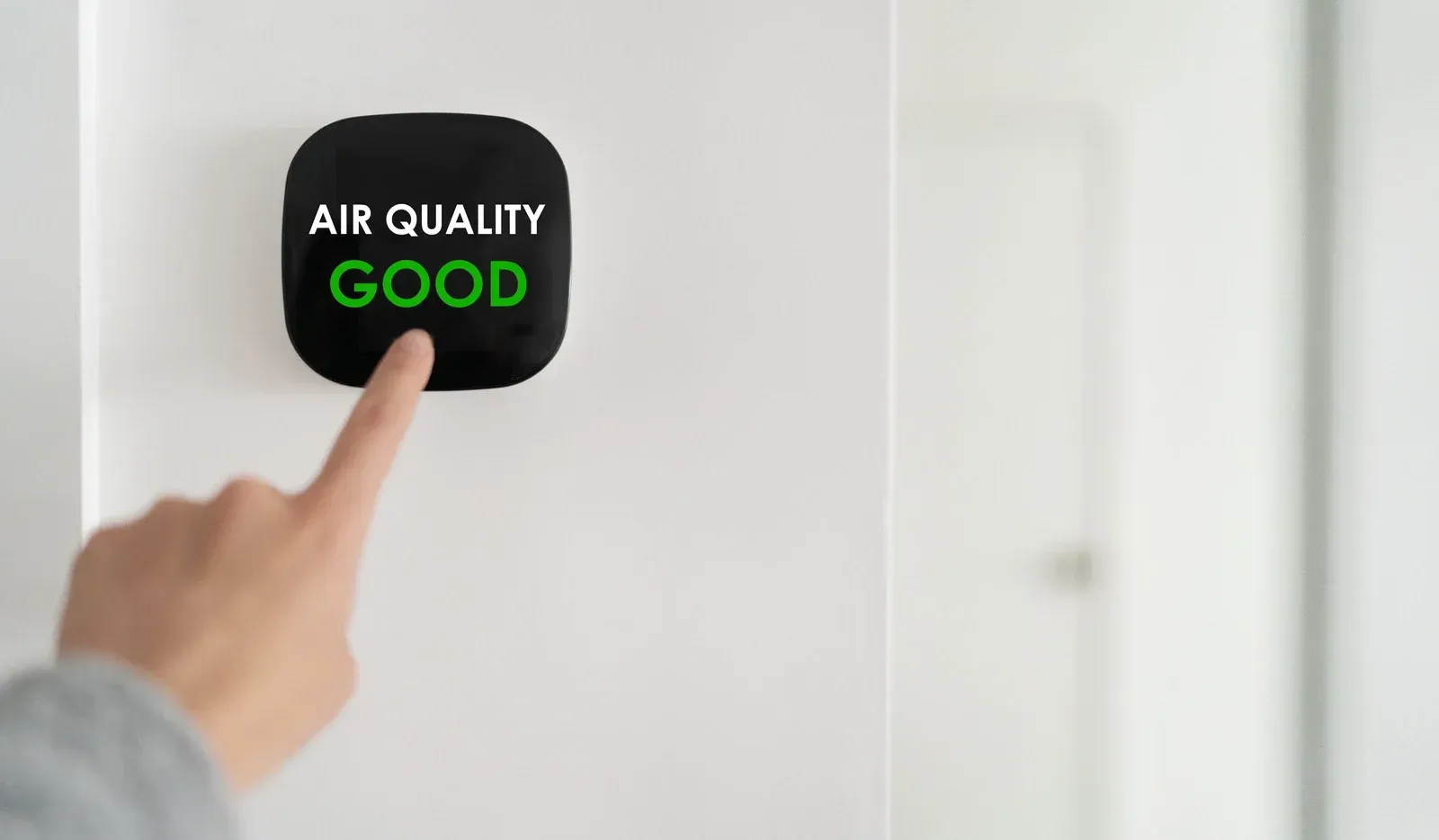 Finger pointing at a black screen showing “AIR QUALITY GOOD” in green text.