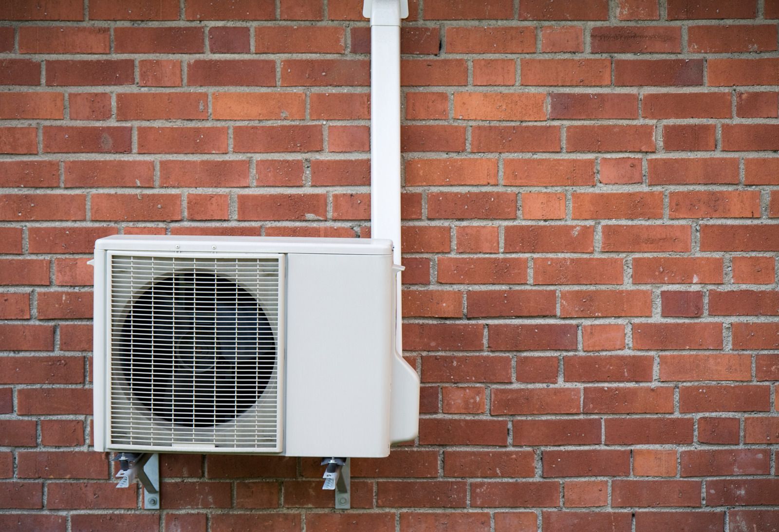 Outdoor air conditioner unit mounted on a red brick wall with white piping