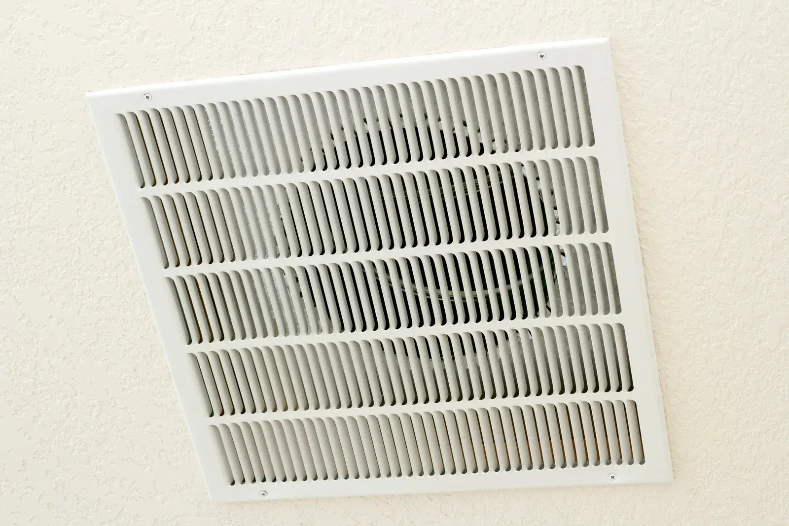 White ceiling air vent grille with horizontal slats on a light-colored ceiling.