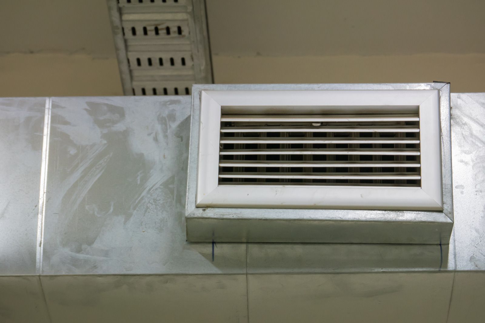 White ventilation vent on a tiled wall near the ceiling