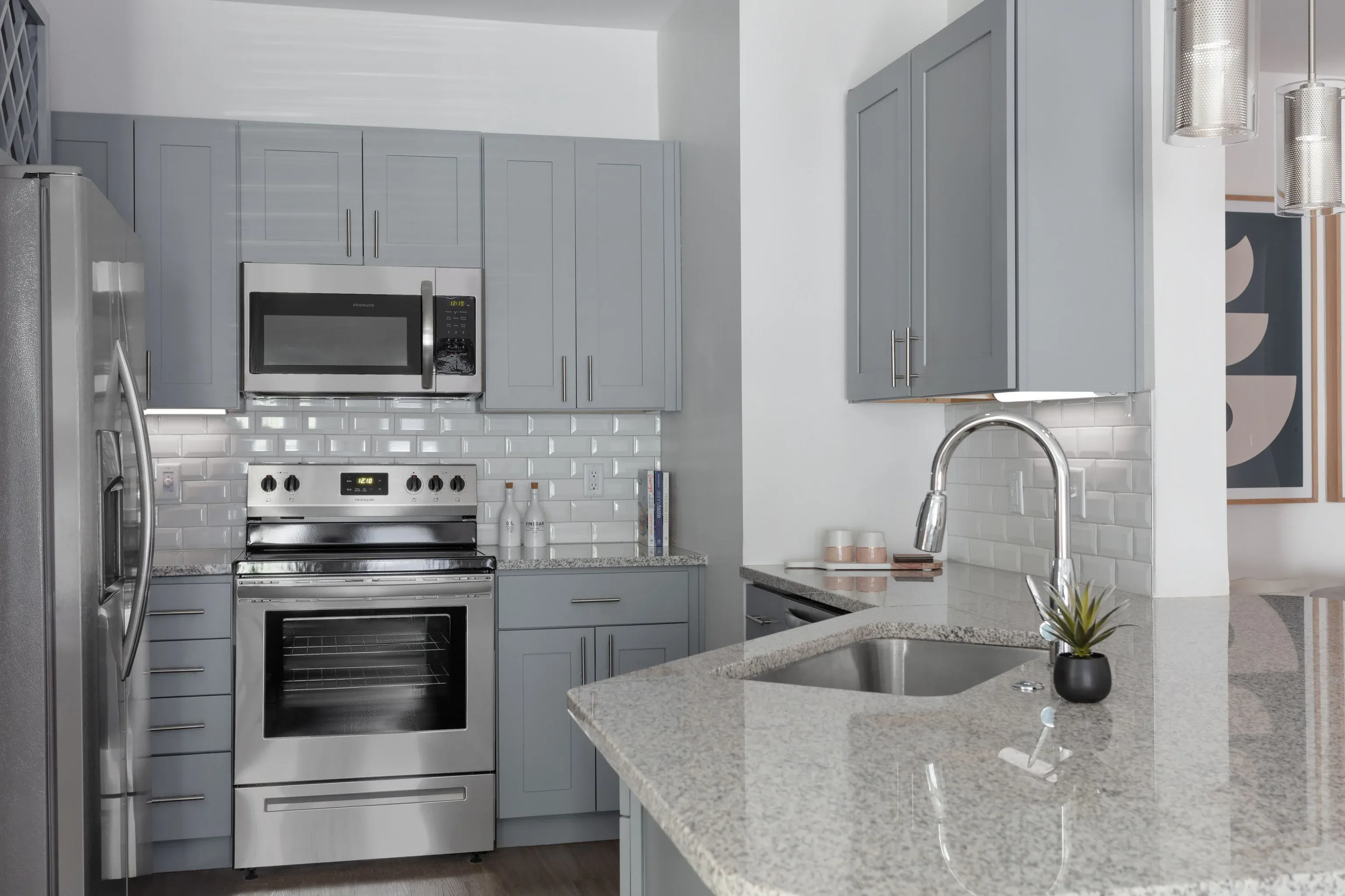 Modern grey kitchen with stainless steel appliances, granite island, and white subway tile backsplash.