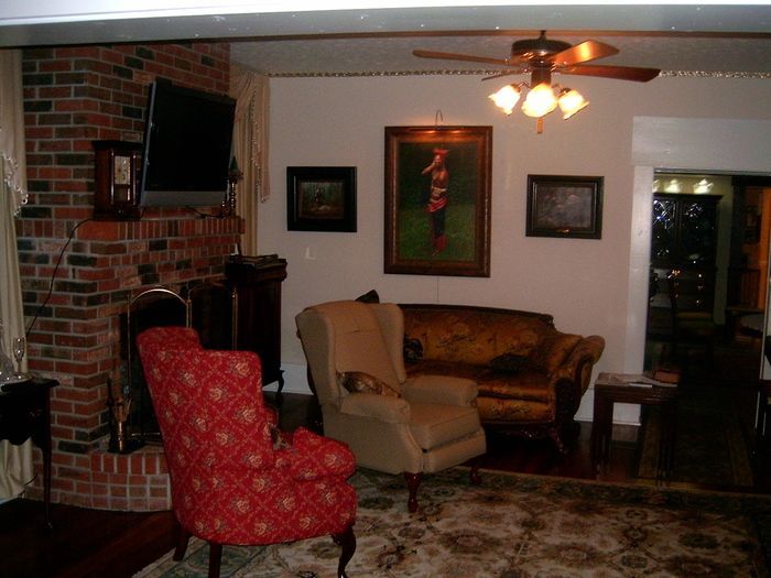 Living room with brick fireplace, red patterned armchair, beige armchair, velvet sofa, art, rug.