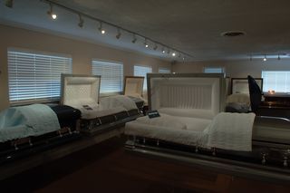 Showroom with several open, empty caskets; white and blue bedding.