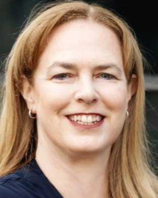 Woman with blonde hair smiling, wearing small hoop earrings.