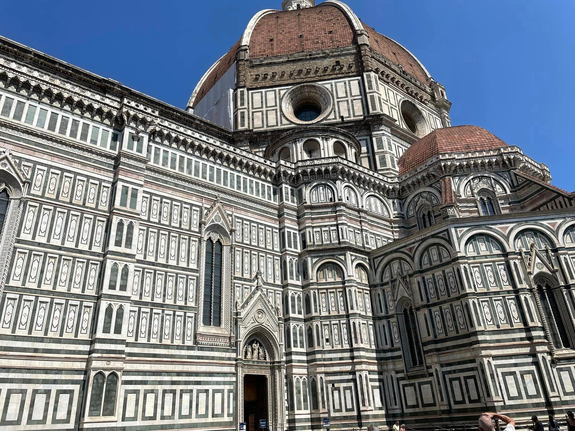 Florence Cathedral, exterior. Multi-colored marble facade with large dome against blue sky.