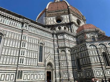 Florence Cathedral, exterior. Multi-colored marble facade with large dome against blue sky.