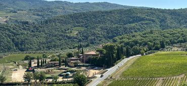 Scenic view of a green Tuscan landscape, featuring rolling hills, vineyards, and a road.
