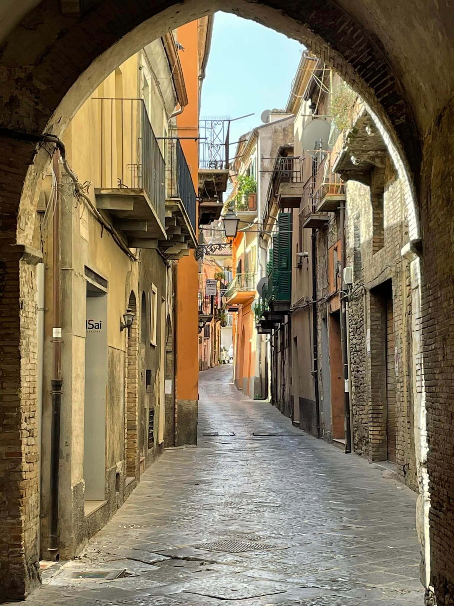 Narrow cobblestone street in an arched passage, lined with aged buildings in warm tones.