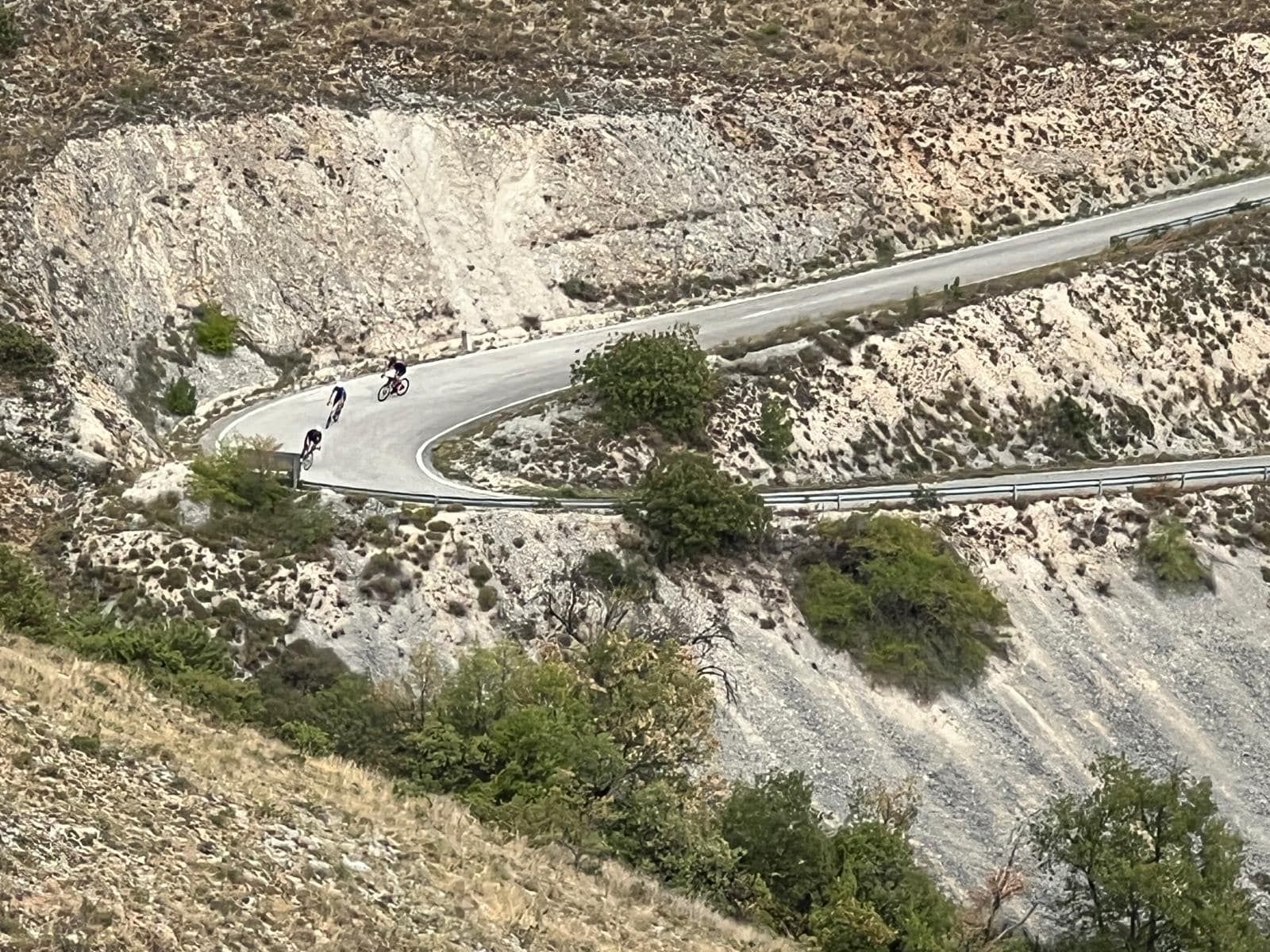 Cyclists riding along a winding road cut into a mountainside.