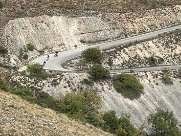 Cyclists riding along a winding road cut into a mountainside.