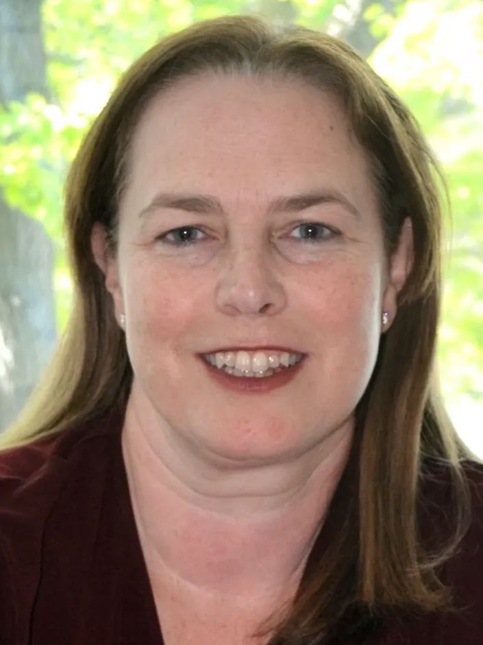 Woman with fair skin, smiling, with long light brown hair, wearing a maroon top.