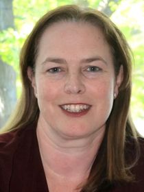Woman with fair skin, smiling, with long light brown hair, wearing a maroon top.