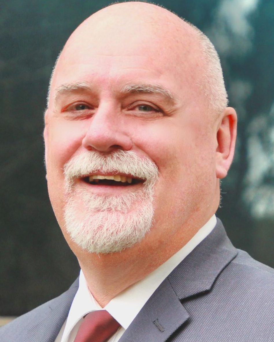 Man in suit smiles at the camera, with a bald head and goatee.