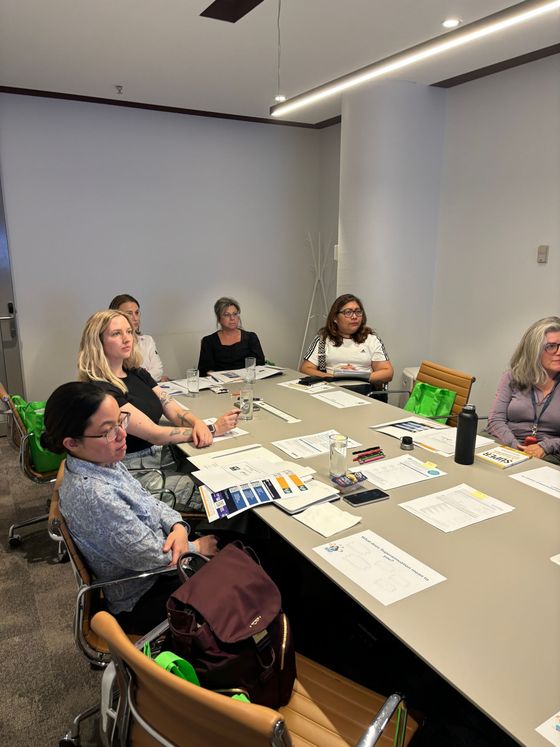People at a table in a conference room, looking at papers; some are smiling or looking at the camera.