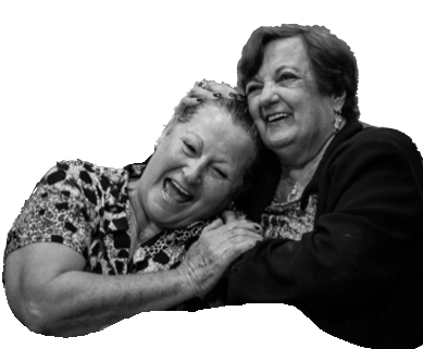 Two elderly women laughing, embracing each other. One rests head on the other's shoulder.