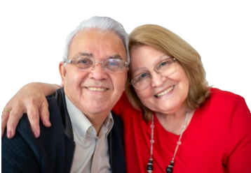 Smiling elderly couple, man with arm around woman's shoulders, indoors, wearing glasses, white background.