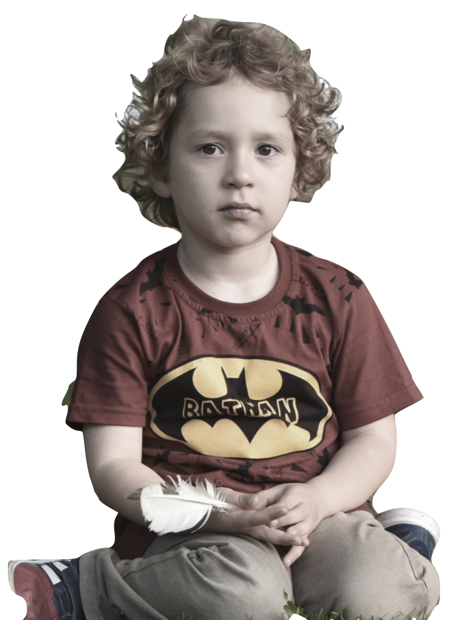 Boy with curly hair wearing a Batman shirt, sitting with a feather.