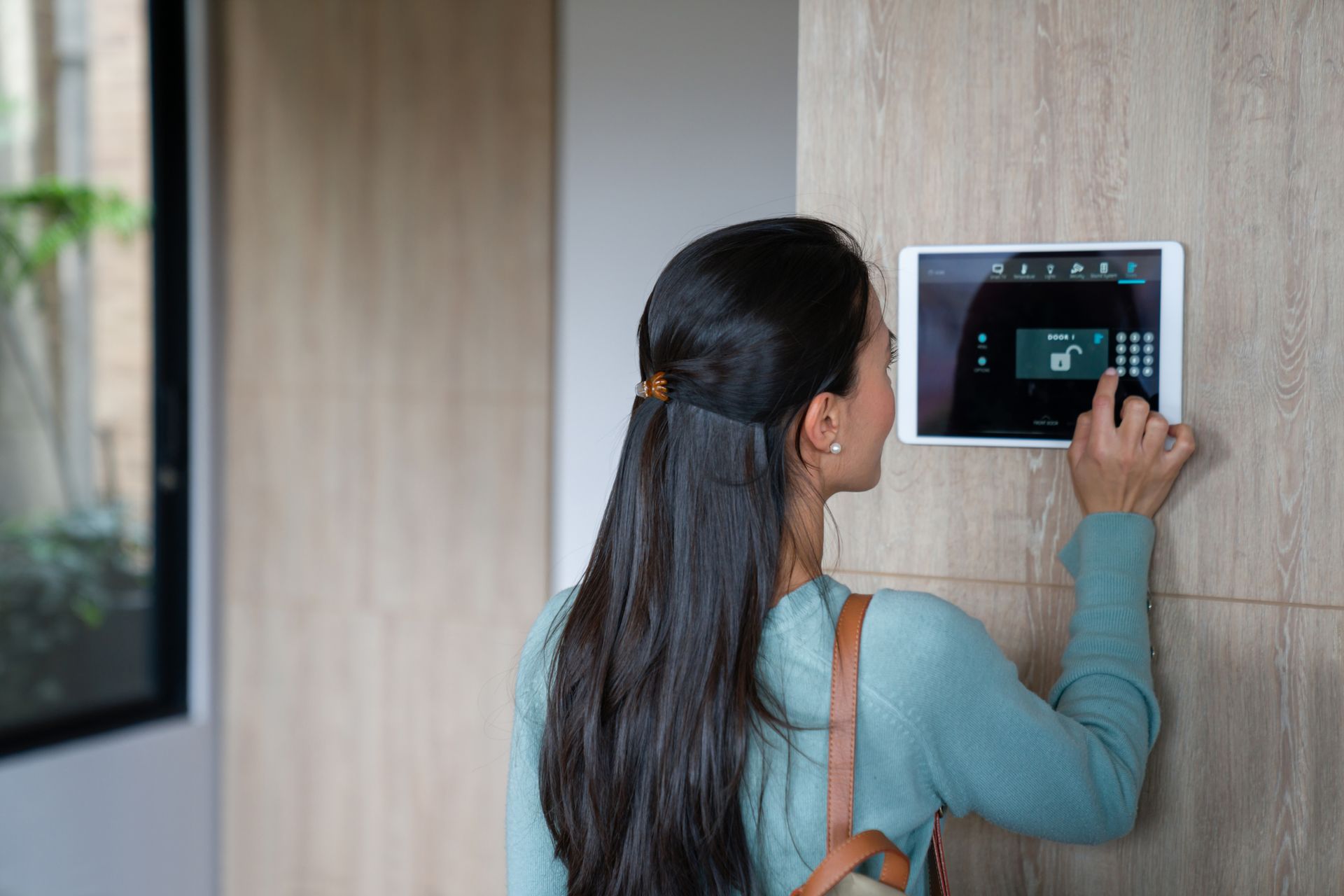 Woman using home security systems keypad to lock front door with smart home automation technology.