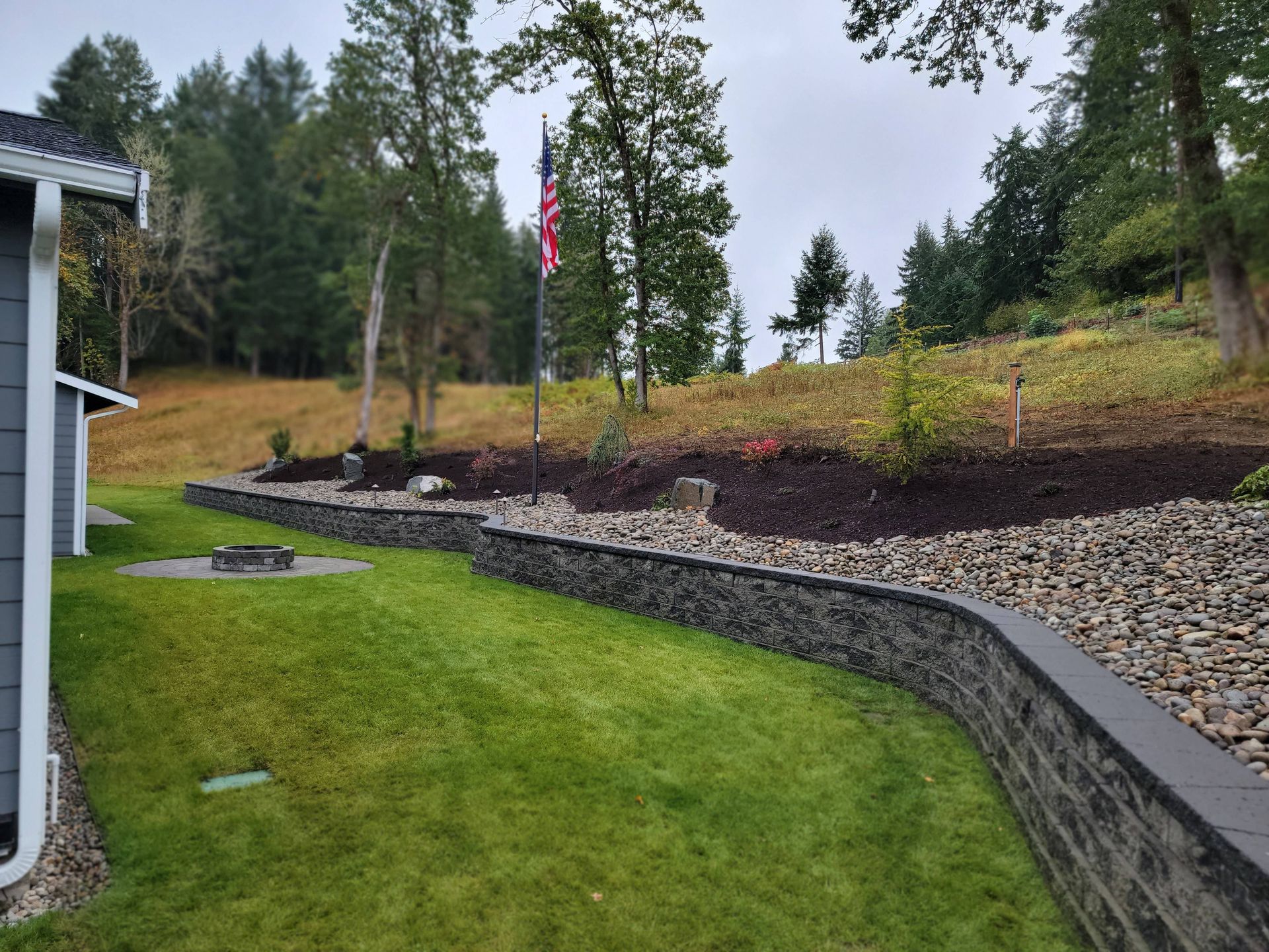 A stone wall surrounds a lush green lawn in front of a house.
