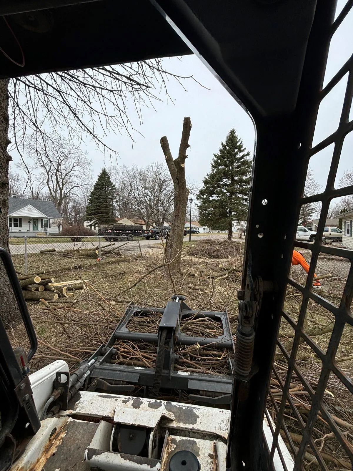 View from inside a skid steer loader; a tree stump and branches are visible in a yard.