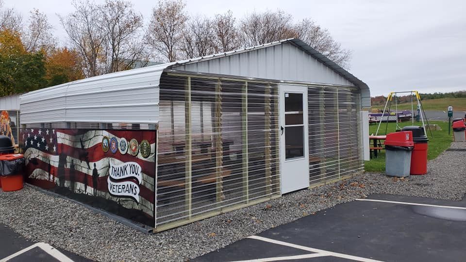 Small greenhouse with slatted sides and white door beside a parking lot