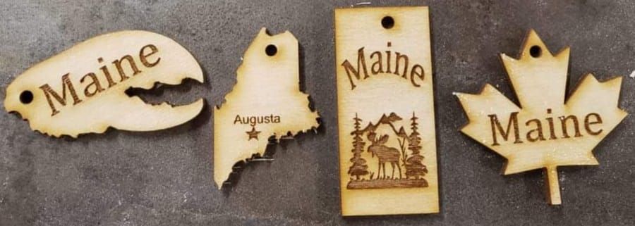 Four Maine-shaped wooden ornaments with carved and painted state designs on a light background