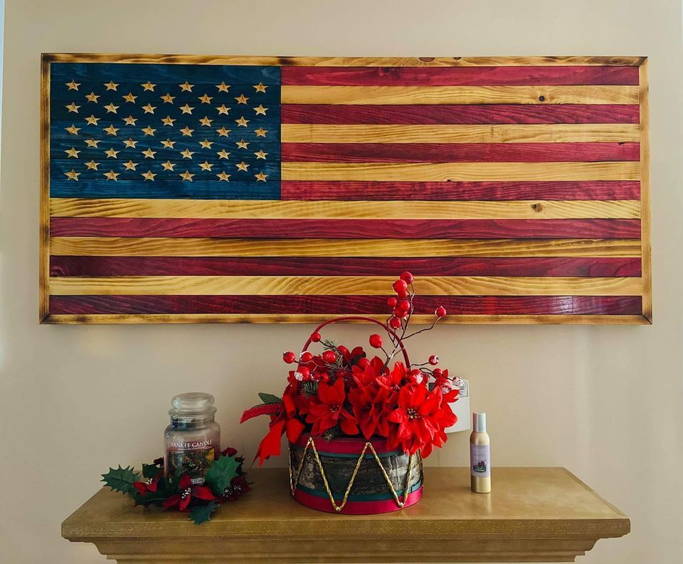 Rustic American flag wall art above a table with red flowers and small decorations
