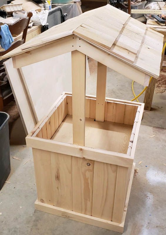 Wooden doghouse under construction with a pitched roof in a workshop setting