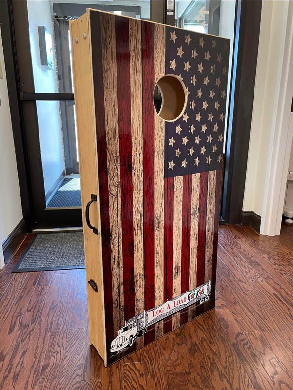 American flag-themed cornhole board standing indoors on a hardwood floor.