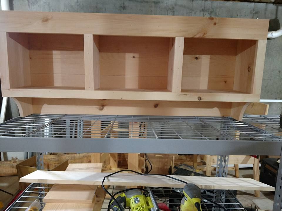 Wooden shelf frame on a metal rack in a workshop, with tools and boards below.