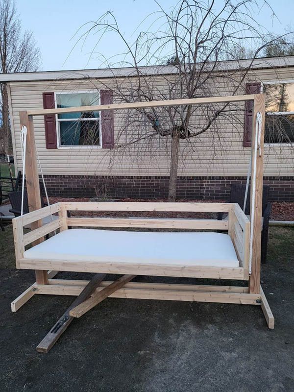 Outdoor wooden bed frame and platform bench with white mattress-like surface in front of a building