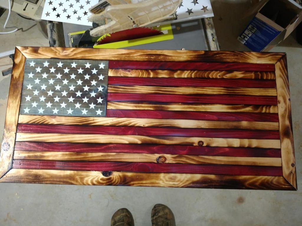 Rustic wooden American flag plaque with stars and red-and-gold stripes on a workbench.