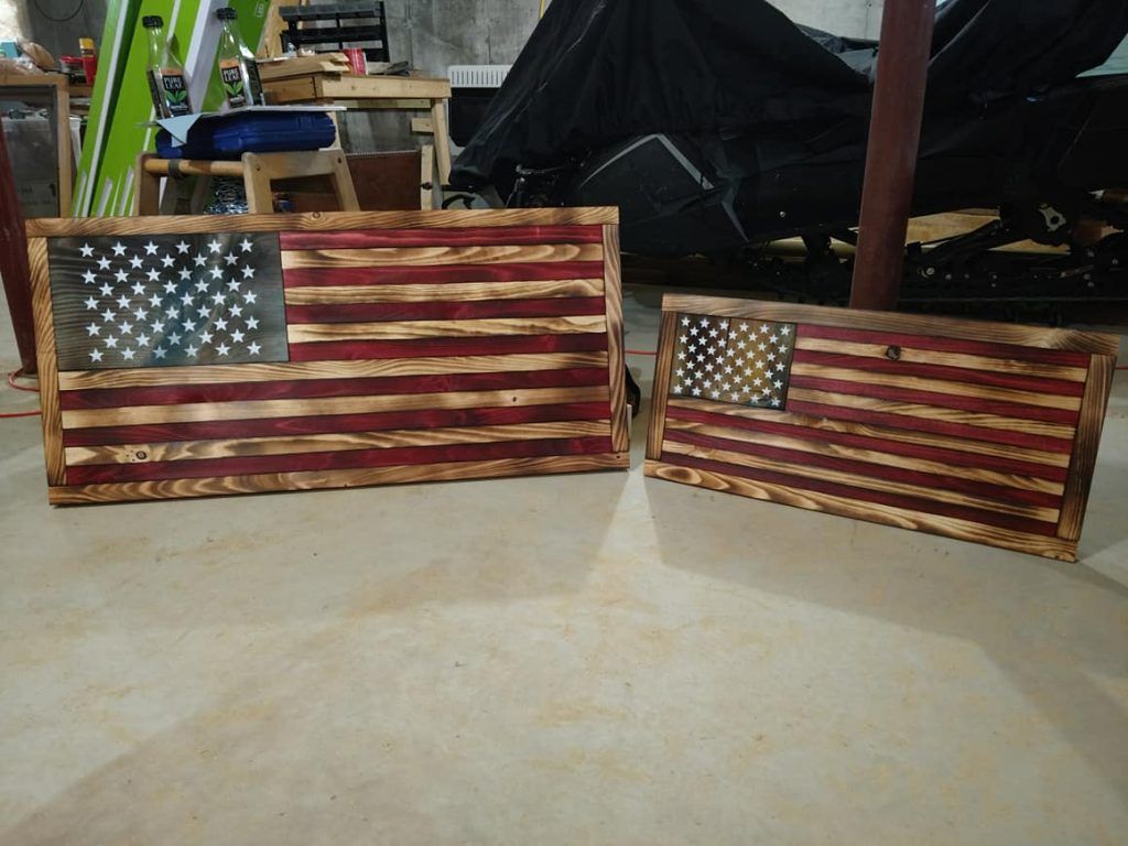 Two rustic painted wooden American flag signs leaning on a workshop floor.
