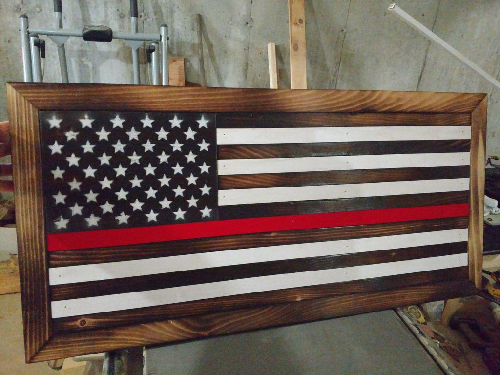 Wooden American flag wall art with stars, stripes, and a red line on a workshop floor