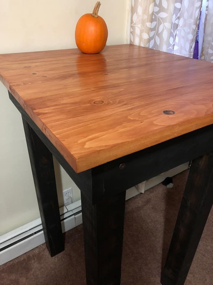 Small orange pumpkin on a wooden table with black legs by a window