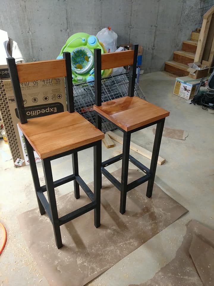 Two wooden bar stools with black metal legs in a workshop, one with a green towel draped over the back.