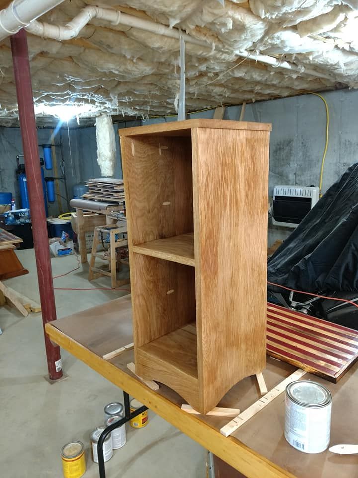 Wooden cabinet under construction in a workshop, resting on a workbench with insulation overhead.