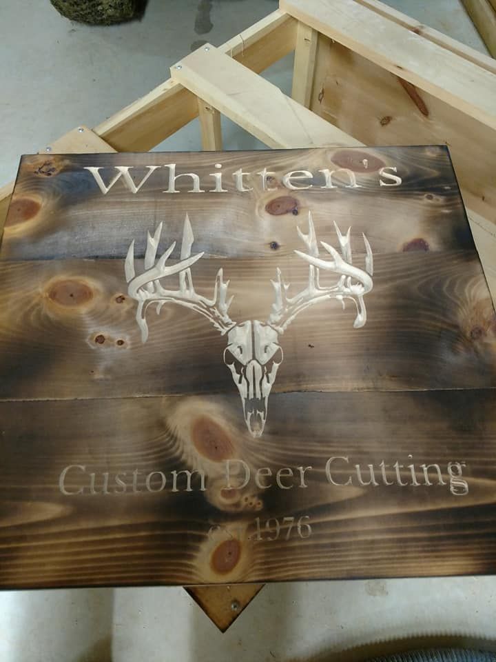 Wooden sign reading “Whitter’s Custom Deer Calling” with white deer antlers and pine knot background