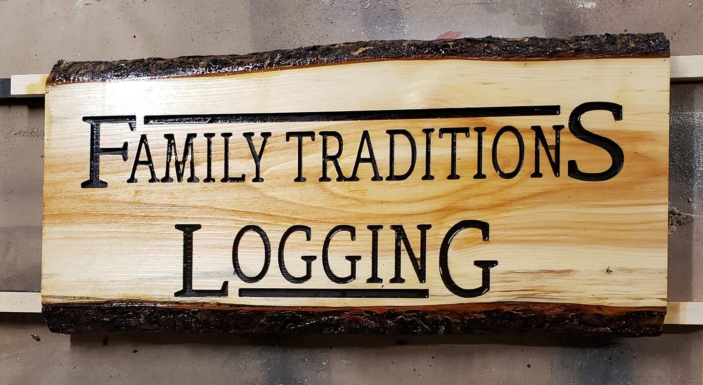 Wooden sign reading “Family Traditions Logging” in black lettering on a light wood background.