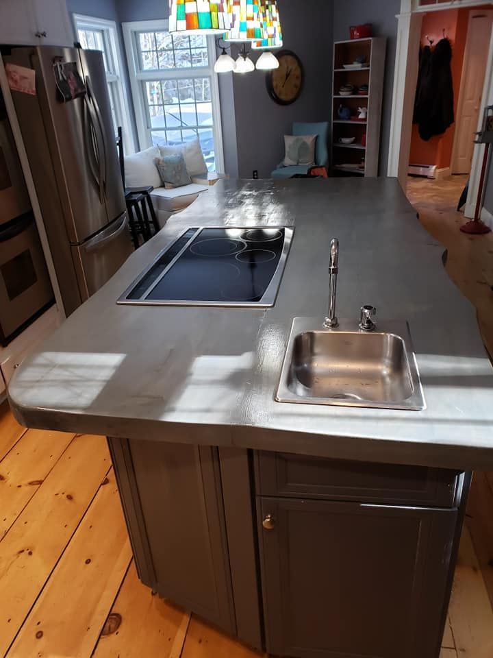 Modern kitchen island with stainless sink, cooktop, and dark cabinets near a bright window