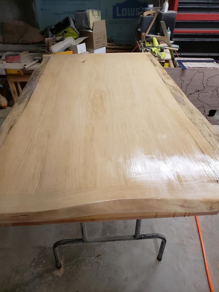 Large unfinished wood tabletop on a metal stand in a workshop, with tools and supplies in the background