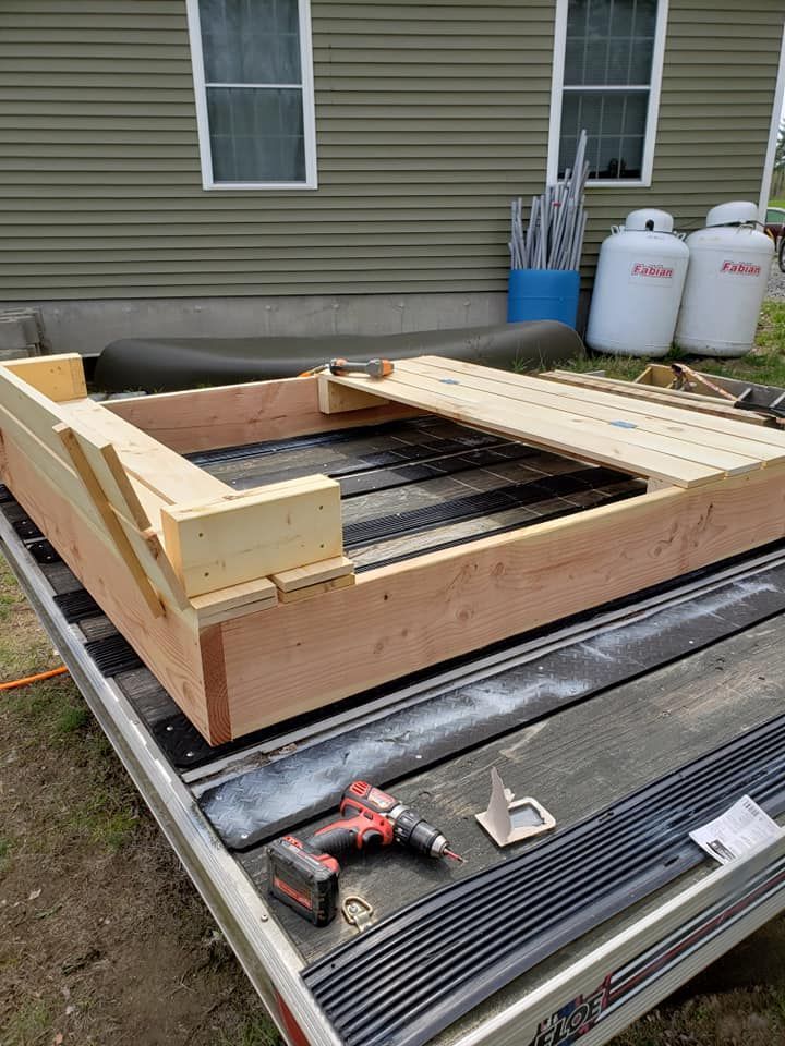 Partially built wooden deck frame on a trailer, with tools and lumber outside a house.