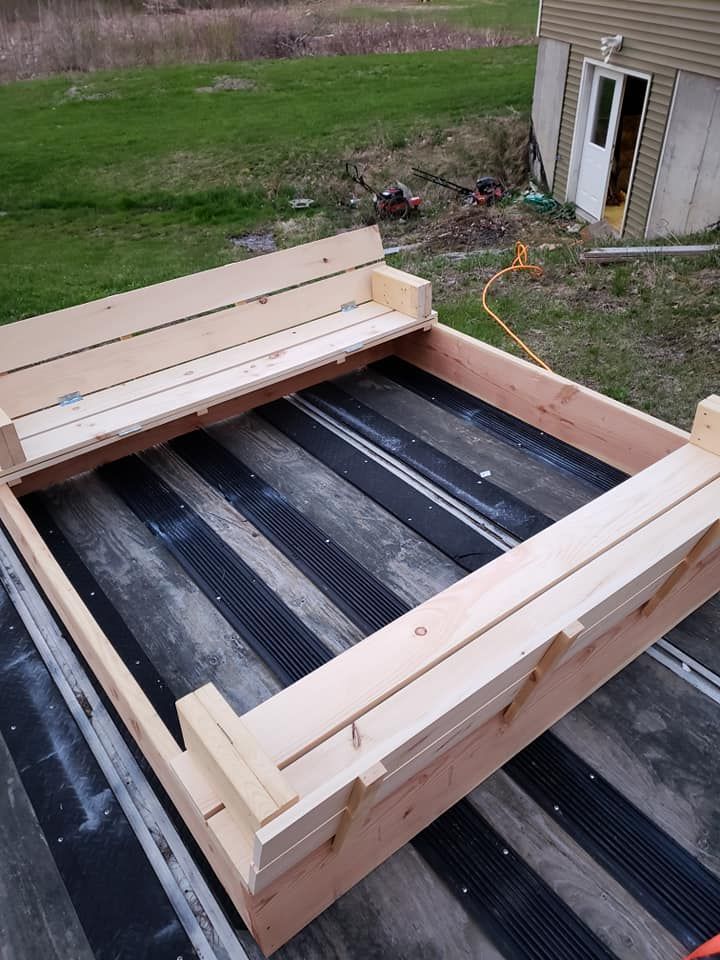 Wooden framed rooftop deck structure under construction beside a house, with black membrane panels inside.